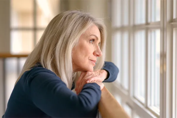 Adrenal-Hormone-Disorder-Clinic A mature woman in a blue shirt looks out the window with melancholy. Schedule treatment for adrenal hormone disorder from Sandra McDonald, NP in Southwestern Ontario.