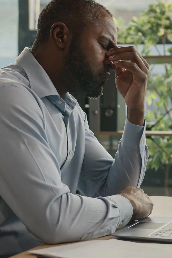 Chronic-Fatigue-Treatment A black man rubbing the top of his nose at his desk, in need of chronic fatigue treatment from Sandra McDonald, NP in Southwestern Ontario.