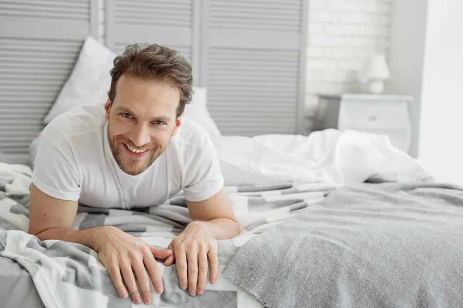 Low-Libido-in-Men-Doctor A dirty-blonde haired man lays on his stomach in bed smiling. Schedule treatment for low libido in men from Sandra McDonald, NP in Southwestern Ontario.