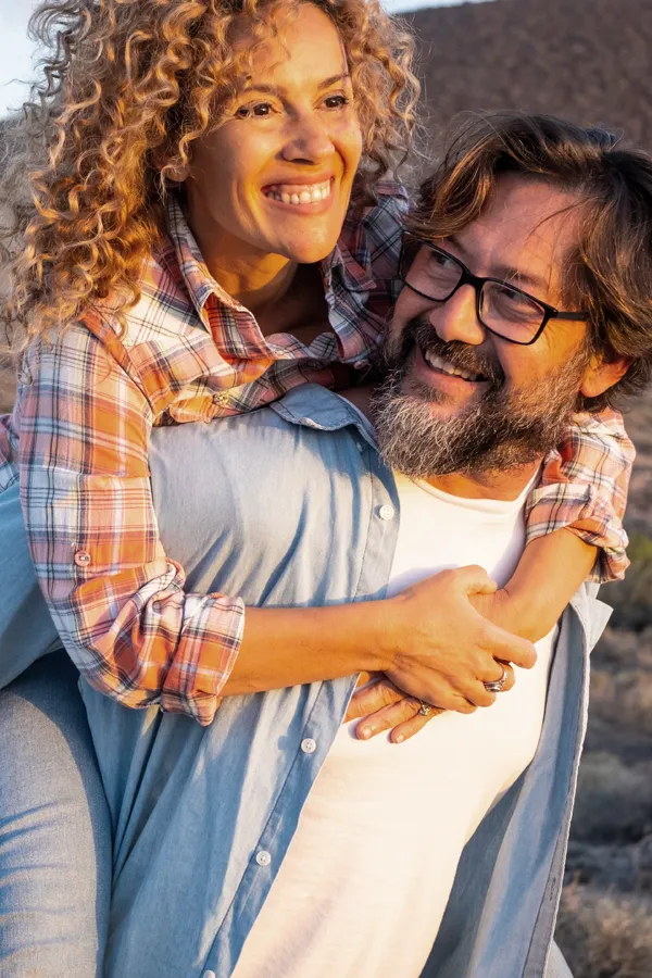 Mental-Health-Treatment A happy woman piggyback rides on her husband on a clear evening. Get mental health treatment from Sandra McDonald, NP in Southwestern Ontario.