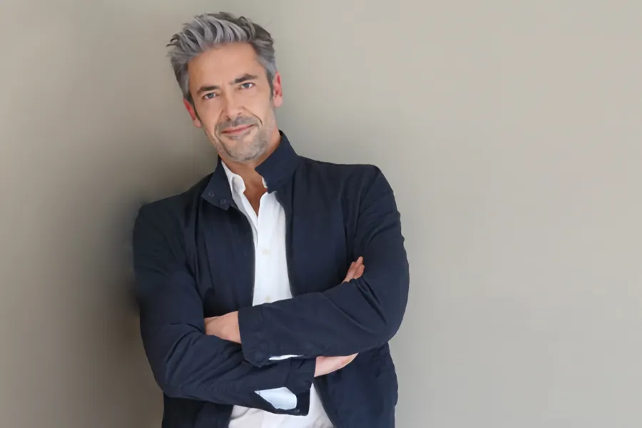 Testosterone-Low-T-Solutionsn-Clinic A middle-aged man in a white shirt and dark blue jacket leans against a gray wall smiling. Get testosterone for Low T from Sandra McDonald, NP in Southwestern Ontario.